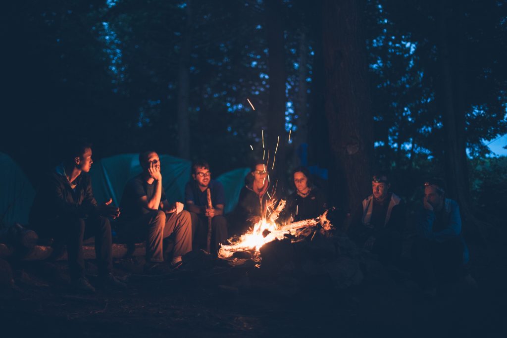 어두운 밤, 산에 캠핑온 사람들이 모닥불을 피워놓고 둘러 앉아 있는 모습